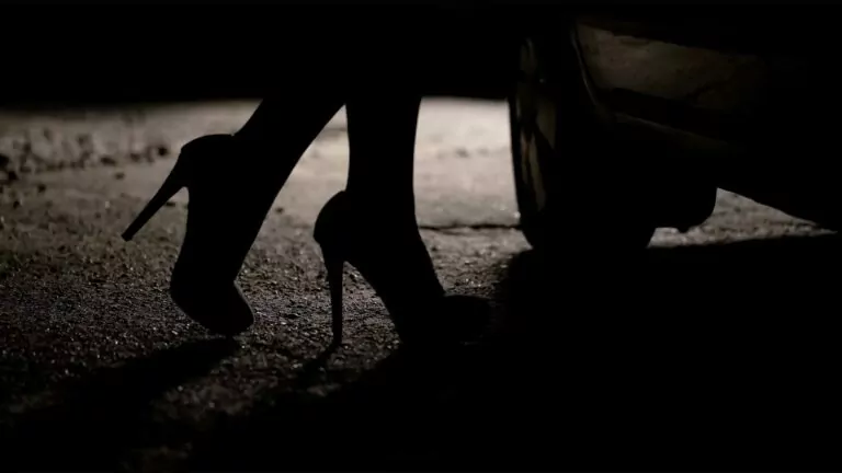 Closeup of a woman's feet in high heels next to a car in the dark.