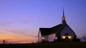 Dusk with sunset and church with steeple and lights in the foreground.